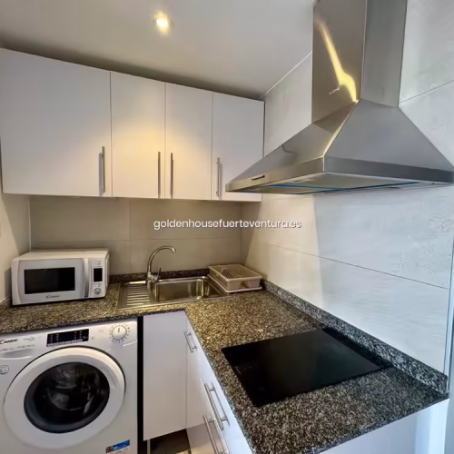 Encimera de cocina con placa vitrocerámica, fregadero de acero y extractor metálico.