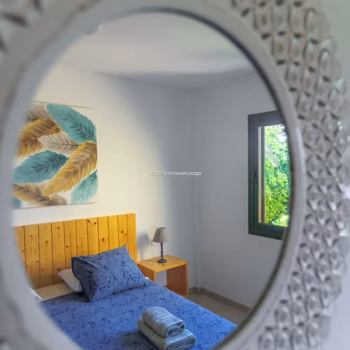 Reflejo del dormitorio principal a través de un espejo circular con marco texturizado.