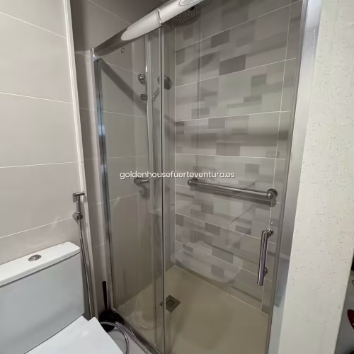 Ducha con revestimiento de azulejos en tonos tierra y mampara de cristal transparente.