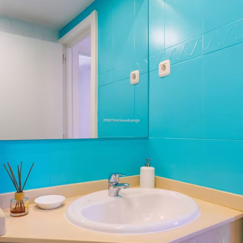 Lavabo sobre encimera en baño con paredes de color turquesa y espejo grande.