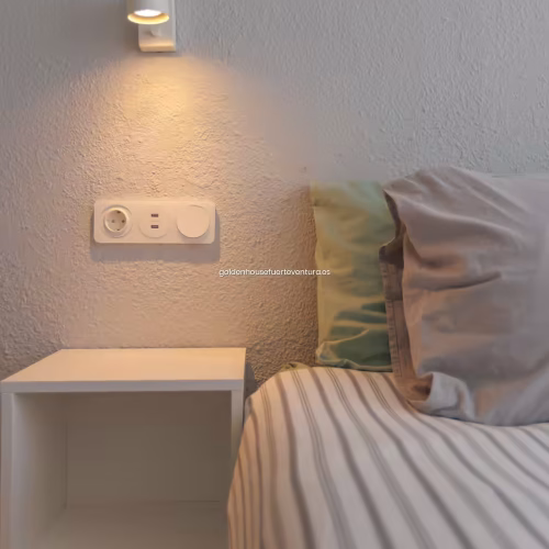 Mesilla de noche cúbica blanca con aplique de pared encendido y base de enchufes con USB