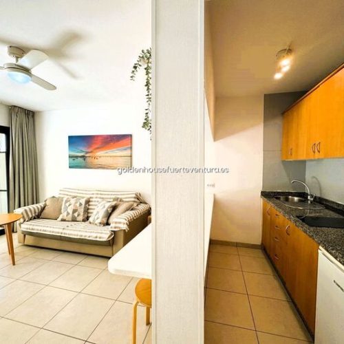 Pared divisoria que separa la cocina de madera de la zona de estar con sofá y mesa.