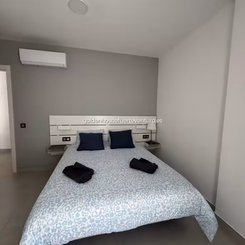 Habitación con cama doble, paredes grises y unidad de aire acondicionado split instalada.