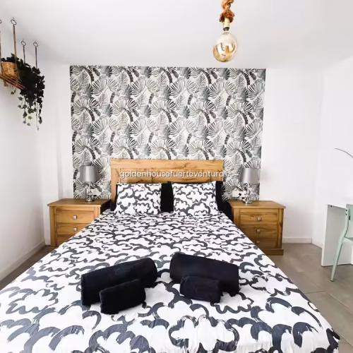 Dormitorio con cama doble, papel pintado de hojas y mesitas de noche de madera en Corralejo.