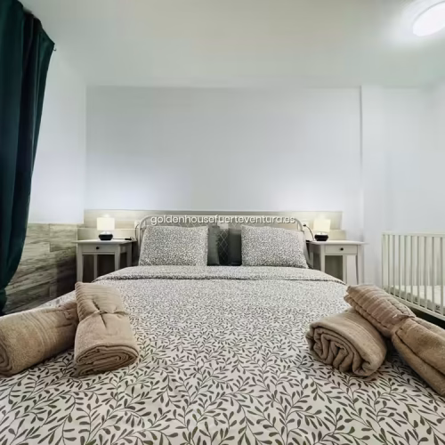 Habitación luminosa con cama doble y cuna blanca de madera lista para huéspedes con bebés.