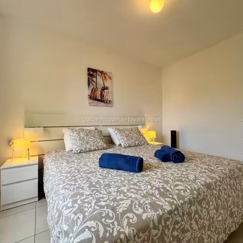 Cama doble con toallas azules y lámparas de noche en Fuerteventura.