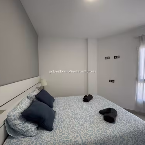 Habitación con cama doble junto a ventana con cortinas traslúcidas que permiten el paso de luz.