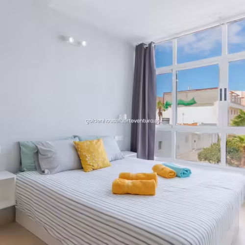 Habitación con cama de matrimonio y amplio ventanal con vistas al exterior bajo un cielo azul