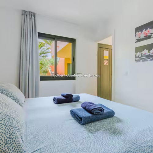Dormitorio con ventana que da al jardín, decorado con cuadros florales y tonos azules.