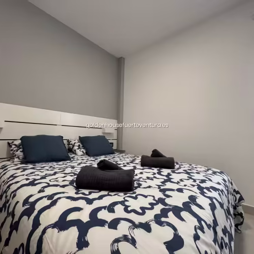 Cama de matrimonio con ropa de cama estampada en azul y blanco y toallas negras cortesia.