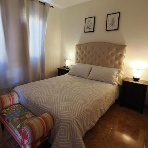 Dormitorio con cama doble, cabecero tapizado y banco a los pies de la cama.