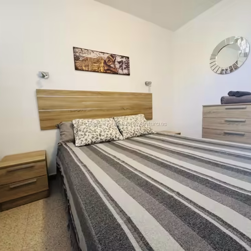 Dormitorio con cama doble, cabecero de madera, mesitas de noche y cuadro decorativo.
