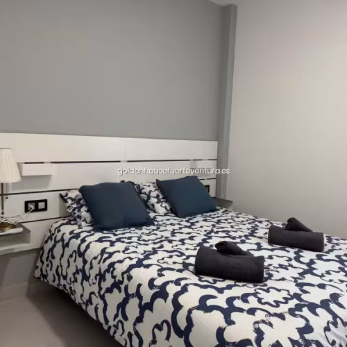 Cama doble con sábanas de patrón azul y cojines oscuros en dormitorio moderno.