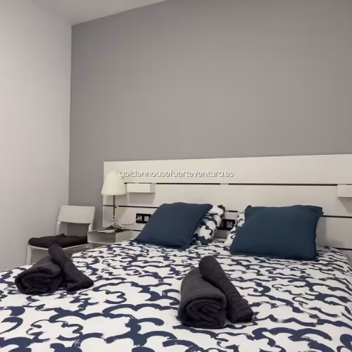 Dormitorio con cama doble decorada con cojines azules y toallas oscuras.