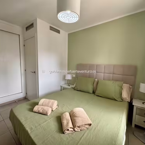 Cama de matrimonio con ropa de cama verde y toallas limpias en apartamento Corralejo.