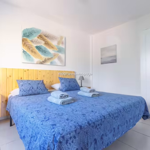 Habitación con dos camas, textiles azules y cuadro decorativo de plumas.