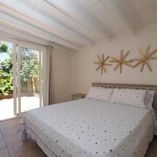 Dormitorio con cama doble, techos altos de madera blanca y salida directa al patio.