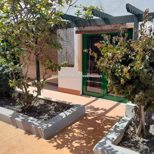 Fachada blanca de estilo canario con jardín de entrada y pérgola oscura.