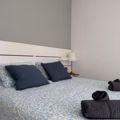 Cama doble con funda nórdica de patrón azul claro y lámpara de mesa clásica.