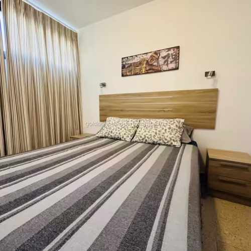 Perspectiva completa del dormitorio con cama de matrimonio y mobiliario auxiliar.