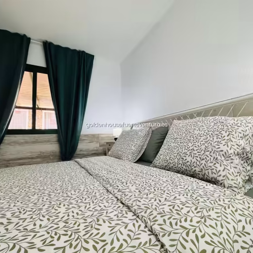 Vista lateral de cama doble con almohadas grandes y cabecero de forja blanco en dormitorio.