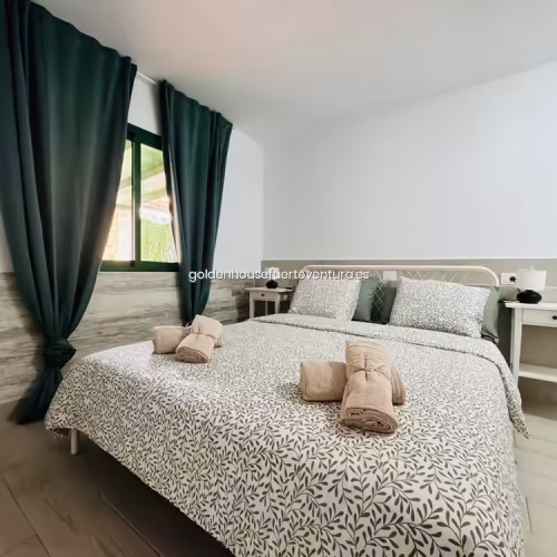 Dormitorio con ventana, cortinas verde oscuro y luz natural en Fuerteventura