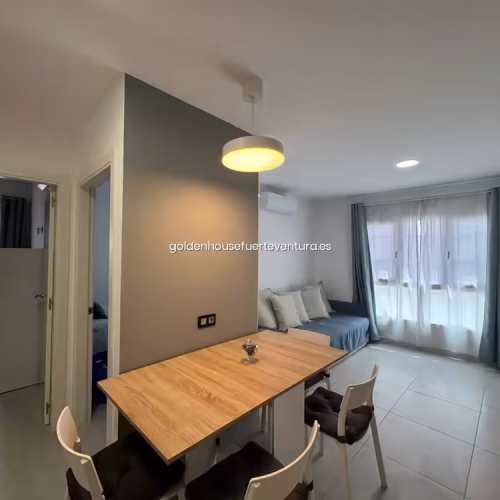 Mesa de comedor de madera clara con cuatro sillas blancas y cojines negros.