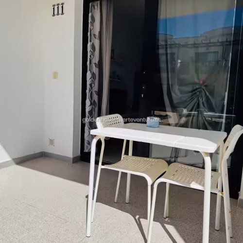 Primer plano de mesa y sillas blancas en la terraza sombreada del alojamiento.