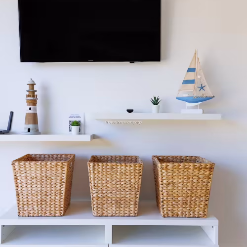 Mueble blanco bajo televisor con cestas de mimbre y adornos de temática marinera.
