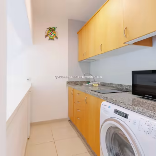 Pasillo estrecho con suelo cerámico que conduce a una cocina lineal de madera.