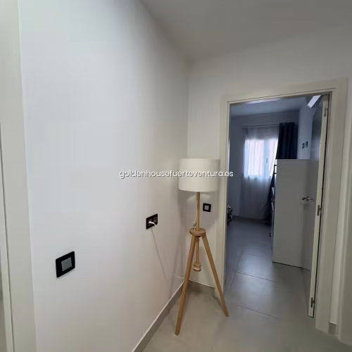 Pasillo de paredes blancas con lámpara de pie tipo trípode de madera.