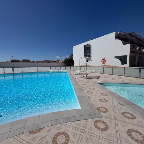 Piscina comunitaria vallada con agua azul y zona de ducha exterior bajo el sol.