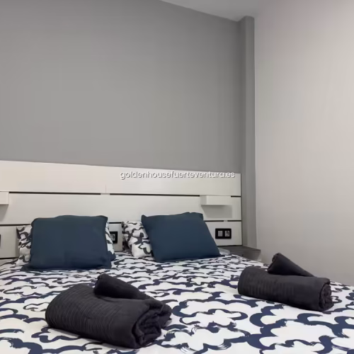 Primer plano de toallas grises enrolladas sobre cama con edredón de patrones azules.