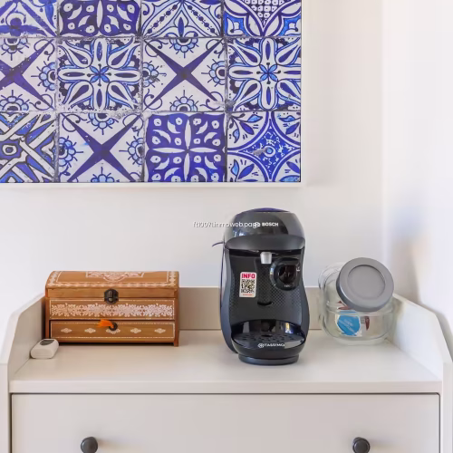 Cafetera de cápsulas Tassimo Bosch sobre mueble blanco con cuadro de azulejos azules.