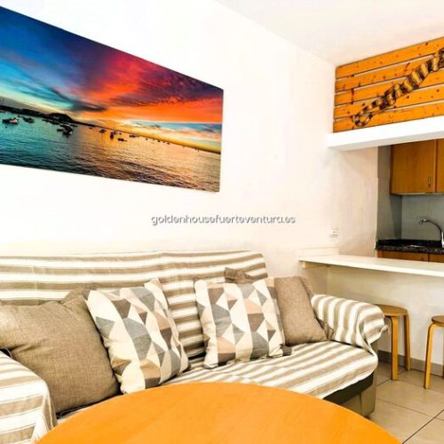 Sofá con cojines geométricos y cuadro de atardecer en el mar en salón de apartamento.