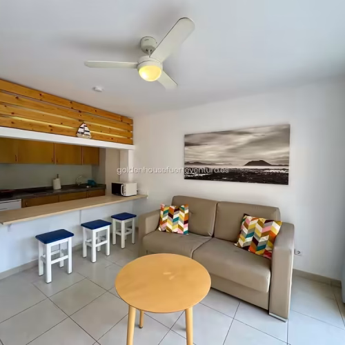 Salón con sofá beige y barra de madera con taburetes en Fuerteventura.