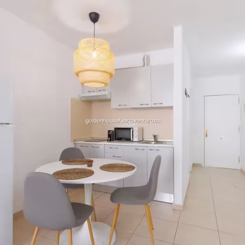 Espacio diáfano con mesa de comedor, nevera blanca y acceso al pasillo de entrada