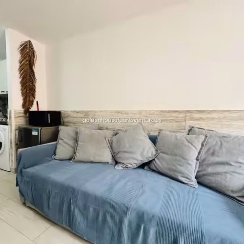 Sofá cama azul y cocina compacta blanca con lavadora integrada.