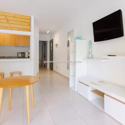 Salón con muebles blancos, televisión y barra de madera con taburetes.