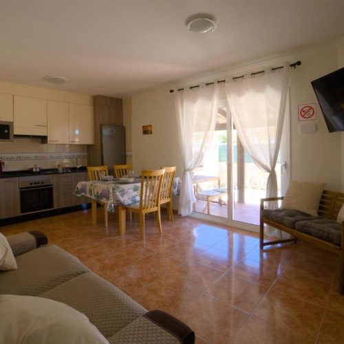 Espacio abierto que combina salón con sofá, mesa de comedor y cocina equipada.