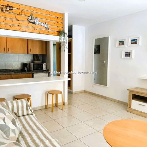 Salón con sofá cama y barra de cocina con taburetes de madera.