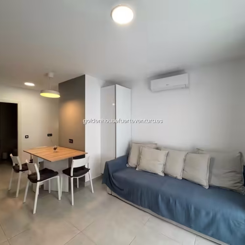 Salón con sofá azul, cojines grises y mesa de comedor de madera.