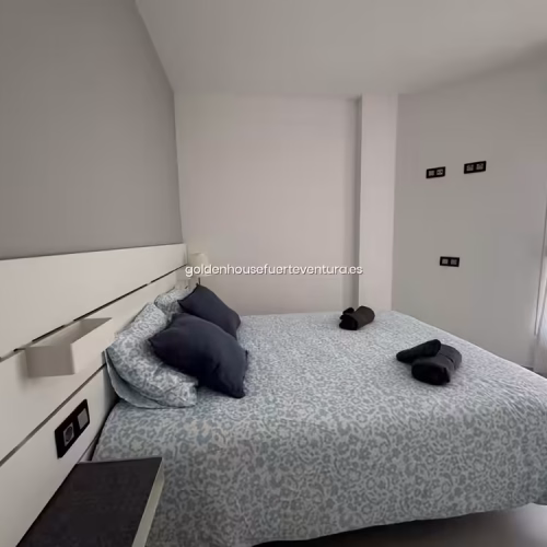 Cama doble con sábanas de estampado celeste cerca de una ventana con cortinas blancas.