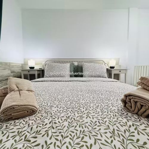 Cama doble preparada con juegos de toallas de cortesía enrolladas para los clientes.