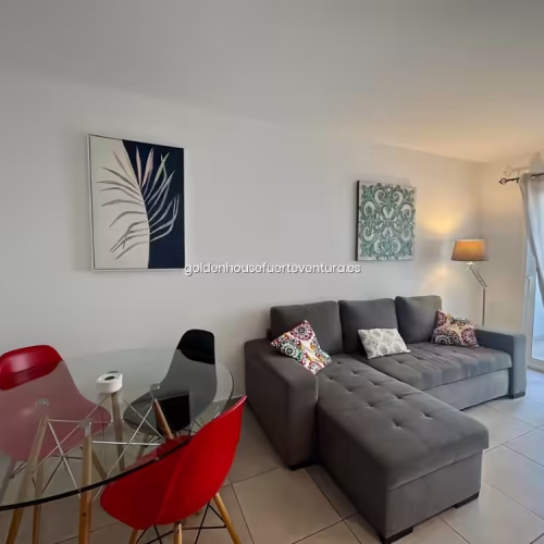 Sofá gris tipo chaise longue con cojines decorativos y cuadros botánicos.