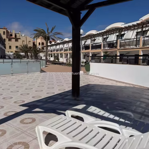 Amplia terraza comunitaria con baldosas decoradas, hamacas blancas y pérgola de madera.