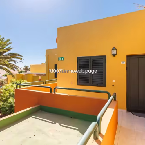 Entrada a vivienda de fachada amarilla con terraza privada y barandilla verde.