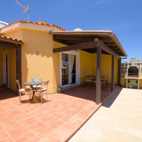 Terraza exterior con mesa de comedor y barbacoa de obra bajo el sol.