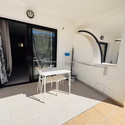 Terraza exterior con mesa blanca, dos sillas y acceso por puerta corredera acristalada.