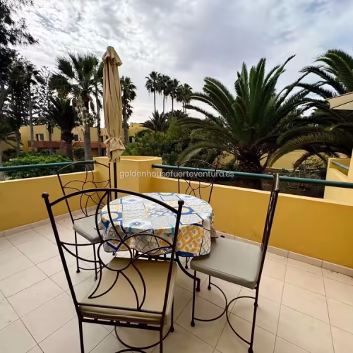Terraza exterior con mesa redonda, sillas de forja y vistas a palmeras en Fuerteventura.